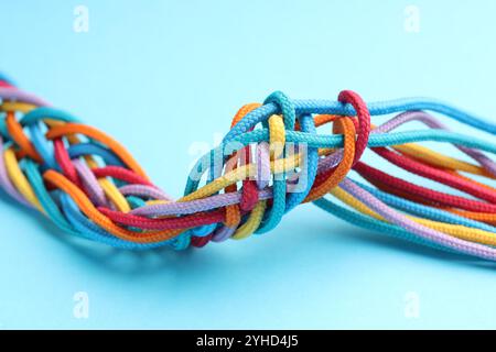 Colorful ropes tied together on light blue background, closeup. Unity concept Stock Photo