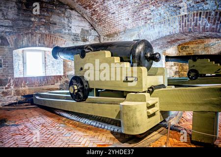 Heavy Cannons inside Fort Monroe Casemate Museum | HAMPTON, Virginia — Heavy naval guns line a brick-vaulted casemate at Fort Monroe's Casemate Museum, mounted on carriages designed to fire through embrasures cut into the fort's massive masonry walls. These smoothbore cannons proved obsolete within a decade of the fort's completion, unable to penetrate the iron plating of ironclads like the CSS Virginia during the 1862 Battle of Hampton Roads, fought in plain view of these ramparts. Stock Photo
