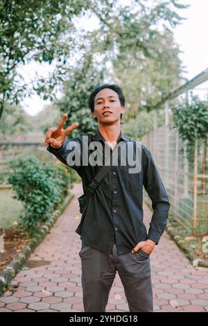 Southeast Asian man showing a peace sign with two fingers, conveying positivity or harmony. Ideal for themes of peace, friendship, or gestures of good Stock Photo