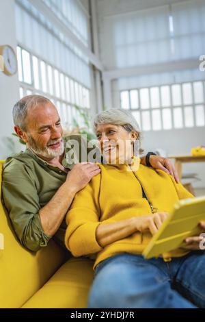Vertical photo of a modern senior couple relaxed at home using digital tablet together Stock Photo