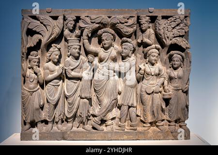 WASHINGTON DC, United States — A schist relief panel from ancient Gandhara depicts the birth of Buddha, with Queen Maya shown in Greco-Roman dress while assuming an Indian nature spirit pose. Created during the Kushan dynasty (late 2nd-early 3rd century CE), this panel was originally part of a stupa's decorative program. The piece exemplifies the cultural synthesis characteristic of Gandharan Buddhist art. Stock Photo