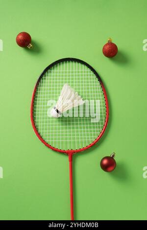 Christmas concept with badminton racket, red balls and white feather badminton shuttlecock on green background. View from above. Xmas card. Stock Photo