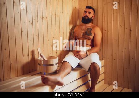 Adult man is relaxing at sauna. Bearded man is sitting in sauna and enjoying healthy treatment. Stock Photo