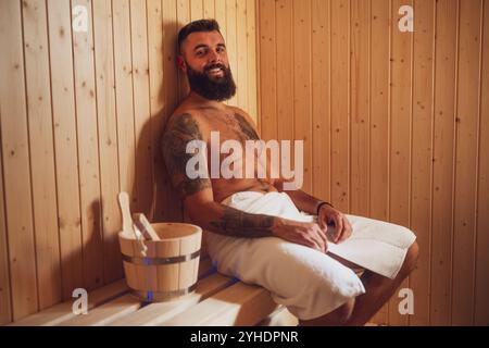 Adult man is relaxing at sauna. Bearded man is sitting in sauna and enjoying healthy treatment. Stock Photo