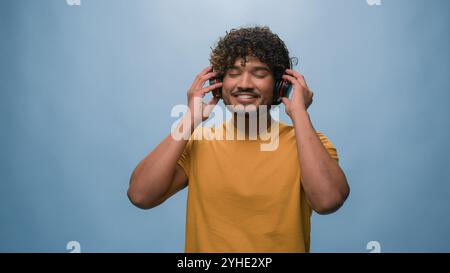 Arabian man happy Muslim guy carefree cheerful joyful Indian male put on headphones dancing listening song listen audio sound dance moving having fun Stock Photo