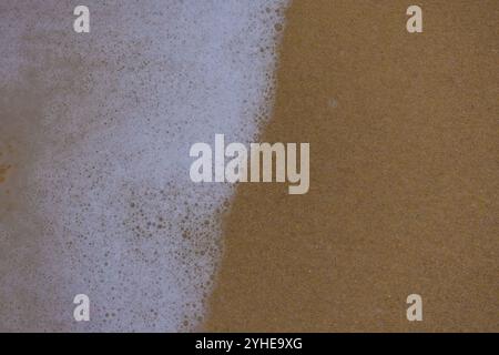 Background close-up of ocean waves rolling on the sand on the beach, with a sand texture. Sandy beach by the sea. A deserted area. Realistic seamless Stock Photo