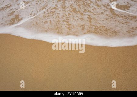 Background close-up of ocean waves rolling on the sand on the beach, with a sand texture. Sandy beach by the sea. A deserted area. Realistic seamless Stock Photo