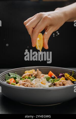 Fresh lemon juice squeezed over a nutritious tuna salad with poached egg, greens and vegetables Stock Photo