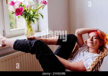 Young woman relaxing in cozy chair by window at home Stock Photo