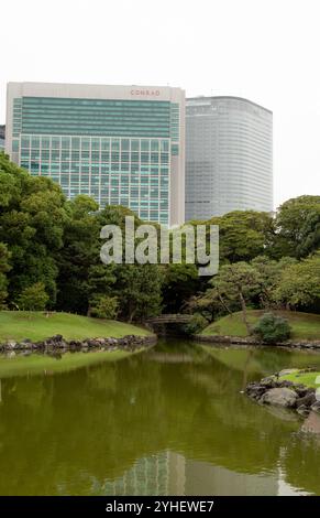 Hamarikyu Gardens in Tokyo Japan include trees and ponds, scenic bridges, and a tea house, all in the middle of urban Tokyo with skyscrapers Stock Photo