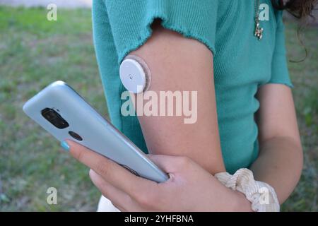 Girl with diabetes is reading the glucose levels from a white sensor on arm using mobile phone application. Modern technology in Medicine Stock Photo