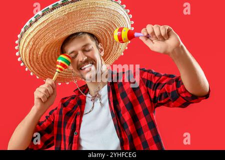 Happy young Mexican man in sombrero and with maracas on red background Stock Photo