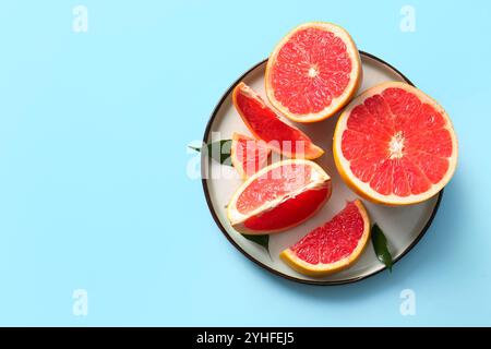Plate with cut fresh grapefruits and leaves on blue background Stock Photo