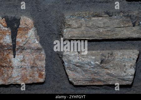 Detailed view of a rustic stone wall featuring varying stone sizes and colors, set against a backdrop of dark, coarse mortar Stock Photo