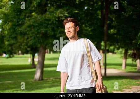 A young Latino man with a beard smiles brightly as he walks through a park, capturing a moment of joy and relaxation in a natural setting. Stock Photo