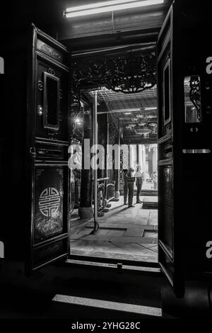 A black-and-white photo of a temple with praying people inside, framed by ornate doors, with light casting shadows on the floor. Stock Photo