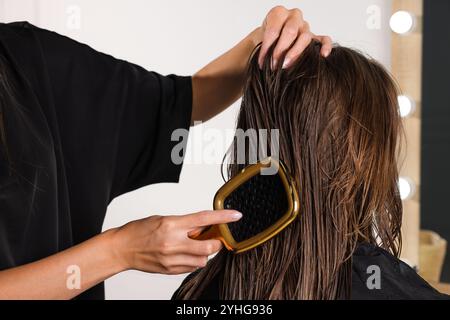 Hairdresser brushing client's wet hair in salon, closeup Stock Photo