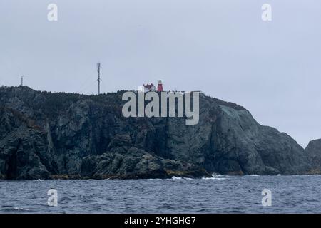 A red lighthouse stands proudly on towering cliffs, with a communication tower to the left, offering a striking contrast between traditional and moder Stock Photo