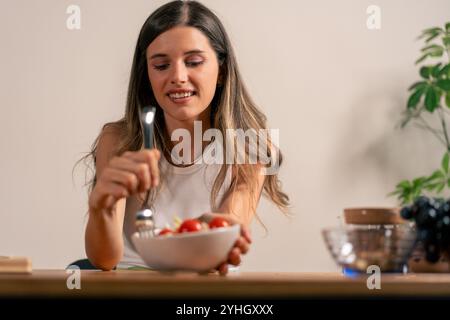 Beautiful young woman enjoying healthy vegetable salad at home, mindful eating and wellness lifestyle moment Stock Photo