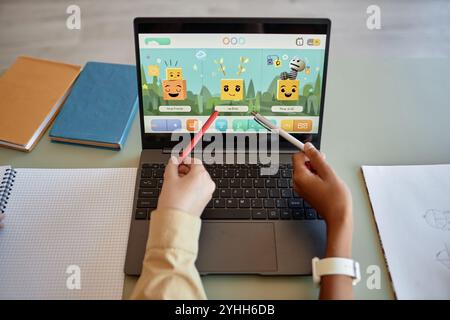 Top view of open laptop with cute characters on screen and two childrens hands pointing working on school tasks together Stock Photo