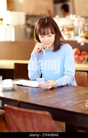 Woman checking her schedule book while looking at her mobile phone in a café Stock Photo