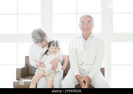 Granddaughter and senior couple sitting on sofa Stock Photo
