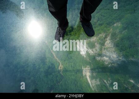 View from Zhangjiajie Grand Canyon glass bridge down to the forest below. Traveler put on shoe cover to protect the glass from getting scuffed by shoe Stock Photo