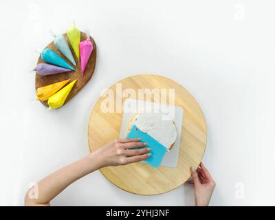 Closeup hand holding plastic cake cream spatula, spread the top of the cake with white cream, creating a decorative pattern on the top of a round cake Stock Photo