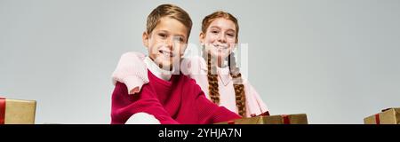Two happy children dressed warmly share smiles while surrounded by colorful presents in winter. Stock Photo