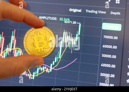 Firenze, Italy November 11, 2024: Trader holding bitcoin coin over digital screen showing positive trading chart, indicating growth and investment pot Stock Photo