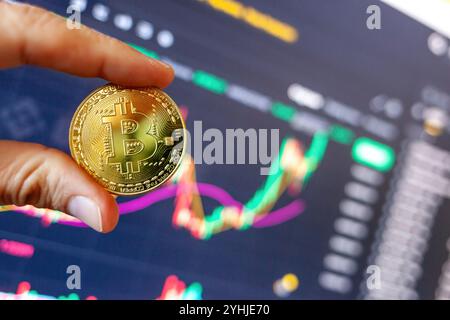 Firenze, Italy November 11, 2024: Trader showing bitcoin cryptocurrency coin in front of rising stock market graph, suggesting successful investment Stock Photo