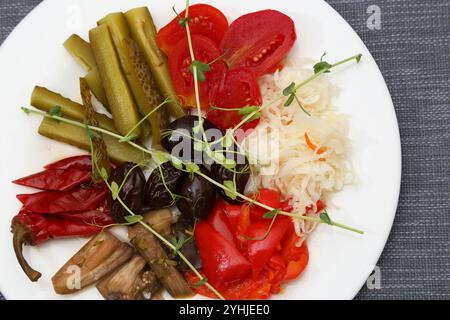 Pickled tomatoes, cabbage, cucumbers, eggplants, paprika, pepper, plums. Pickles on a white plate. Serving various pickled vegetables in a restaurant Stock Photo