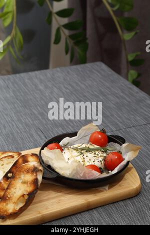 Grilled Camembert cheese with tomatoes and toasted bread. Camembert in a grill pan on a wooden board Stock Photo