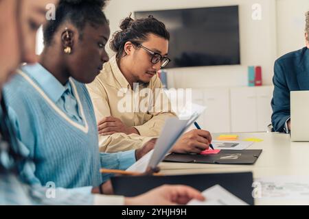 Diverse young professionals reviewing documents together during team meeting showcasing workplace collaboration and focused attention Stock Photo