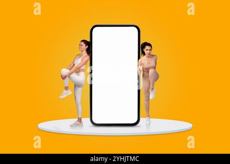 Two women performing fitness exercises next to a large blank smartphone display Stock Photo