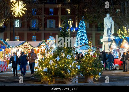 People walking among illuminated kiosks and Christmas trees on the small town square during traditional Christmas market in Asti, Italy. Stock Photo