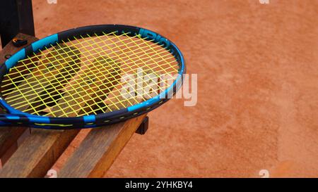 Tennis racket on bench in yellow and blue colors, clay court background Stock Photo