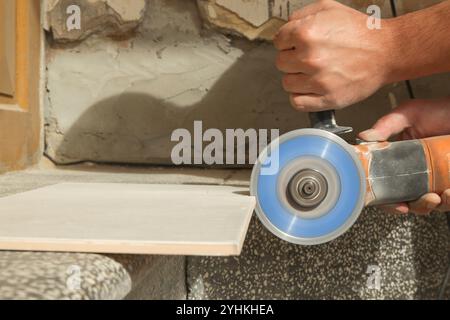 Worker cutting ceramic tile with disc grinder machine. DIY home improvement project. Stock Photo