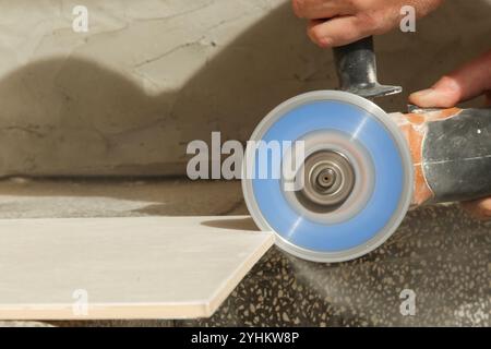 Worker cutting ceramic tile with disc grinder machine. DIY home improvement project. Stock Photo