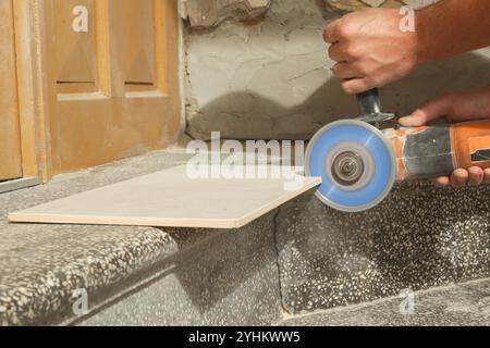 Worker cutting ceramic tile with disc grinder machine. DIY home improvement project. Stock Photo