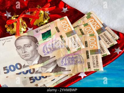 Ukrainian banknotes - hryvnia on the background of the New Year and Christmas decor. Santa Claus hat, bells and stars. Stock Photo