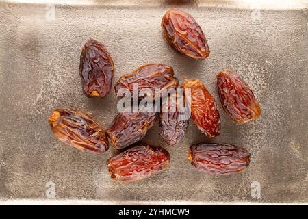 Several sweet dried pitted dates on a metal tray, macro, top view. Stock Photo