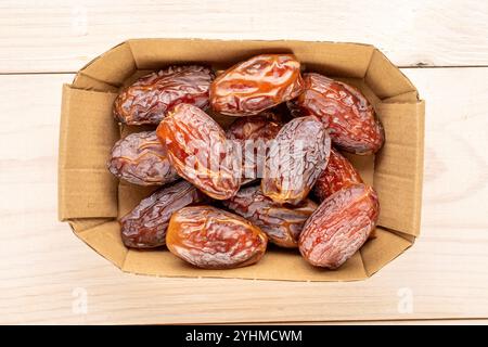 Several sweet dried pitted dates with paper plate on wooden table, macro, top view. Stock Photo