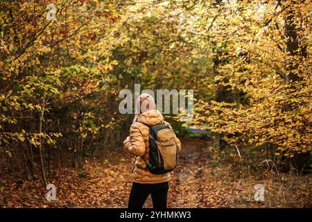Hiking in autumn woodland. Woman with backpack exploring forest at fall season Stock Photo