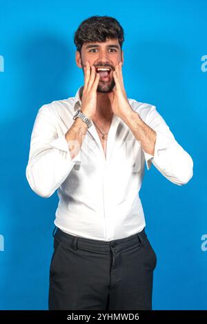 Young businessman shouting with hands on face, expressing excitement and surprise on a vibrant blue background Stock Photo