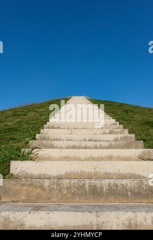 Long Staircase Leading Up a Green Hill Under Blue Sky. Concrete steps leading up a grassy hill on a sunny day. Vertical photo. Nobody, copy space for Stock Photo