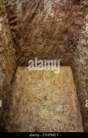 Hand dug deep rectangular hole in the ground, view of grave pit from ...