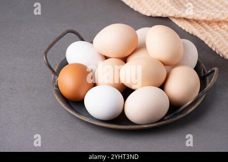 A collection of fresh eggs displayed in a rustic bowl on a textured countertop with a soft cloth in the background Stock Photo