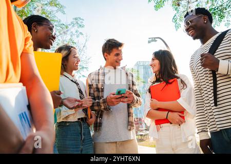 Diverse group of college students talking and laughing together outdoors on campus, friends bonding, sharing ideas, and enjoying casual conversation in a relaxed, university with notebooks and devices. High quality photo Stock Photo