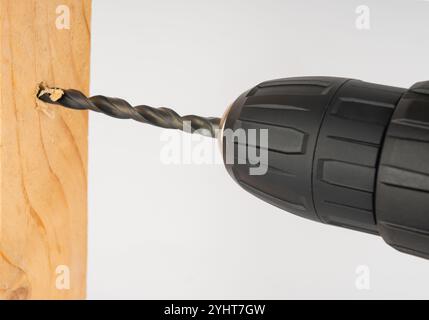 an electric drill drills a hole in a wooden board. Stock Photo